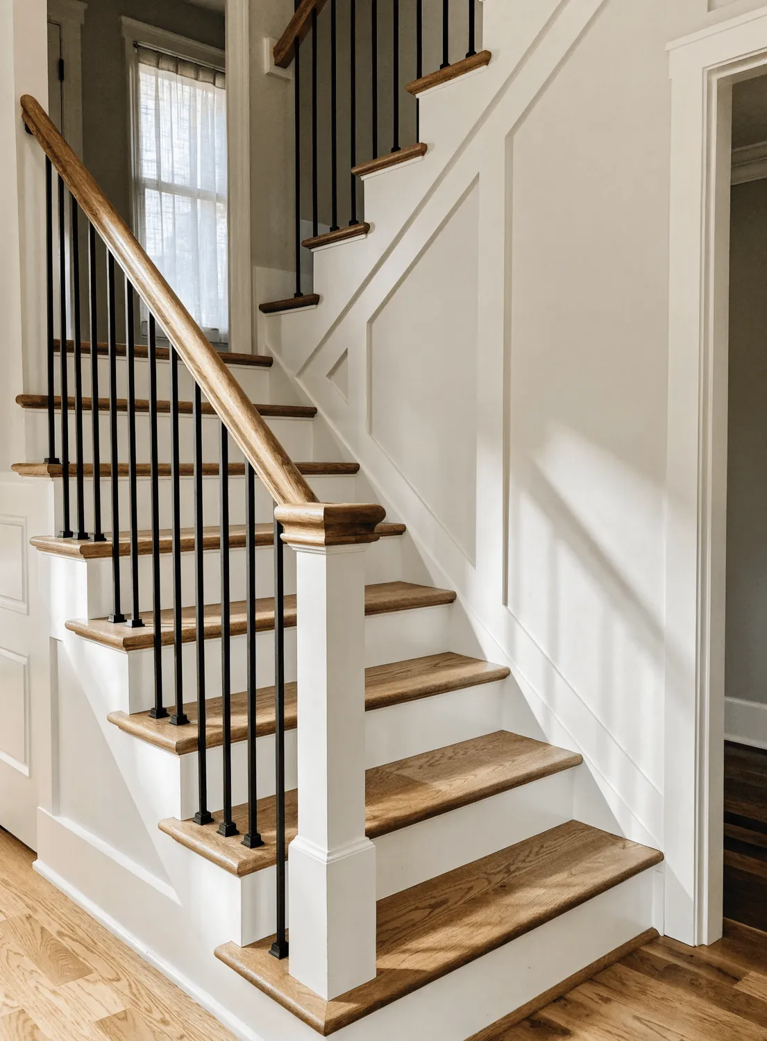 Remodeled staircase with white risers, stained oak treads, an oak handrail, and black metal balusters by Fogg Carpentry
