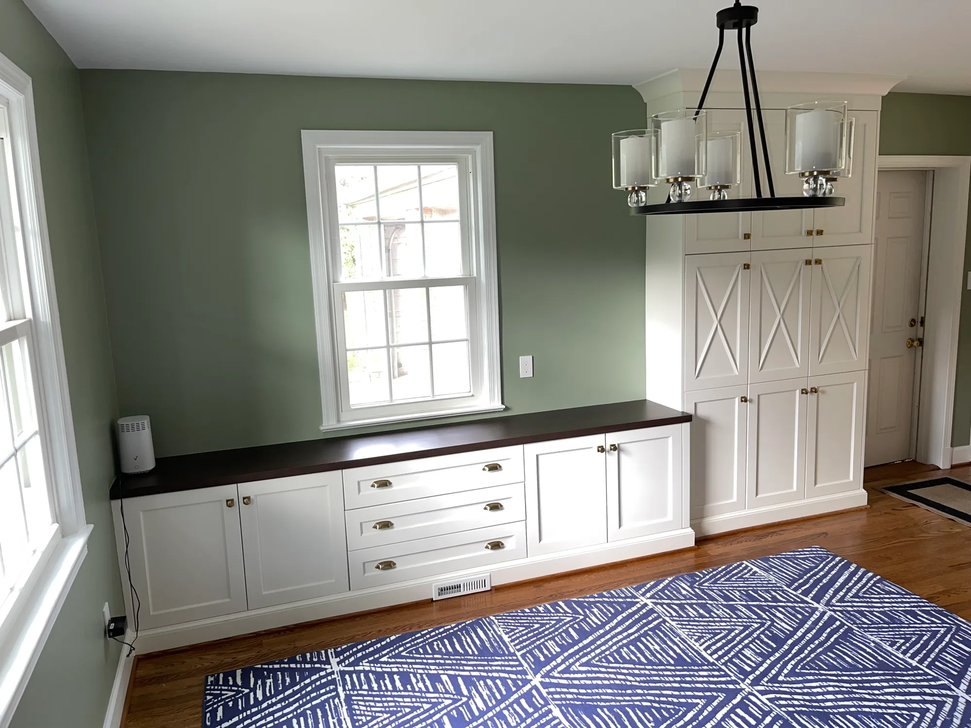 Custom white dining-room built-in cabinetry with a dark wood top under a window by Fogg Carpentry